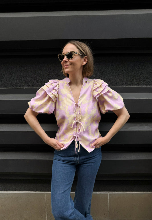 The model in the background of the building wearing a cotton blouse ALIANNA tied at the front and navy blue jeans ATLANTA.