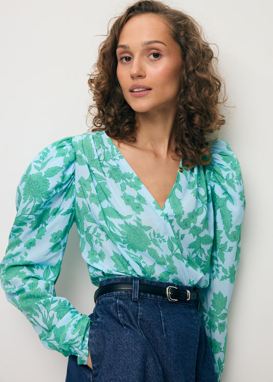 Close-up of a model wearing a blue bodysuit with an original ALIBA print and a BREDA denim mini skirt.
