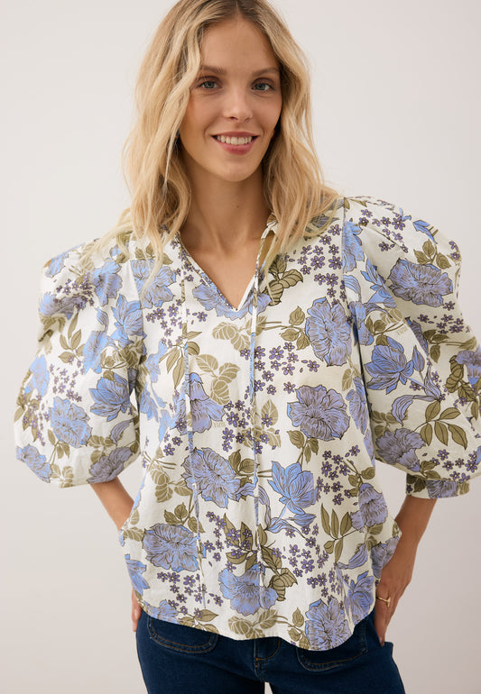 Close-up of the ADRASSA blouse on a model standing against a white wall.