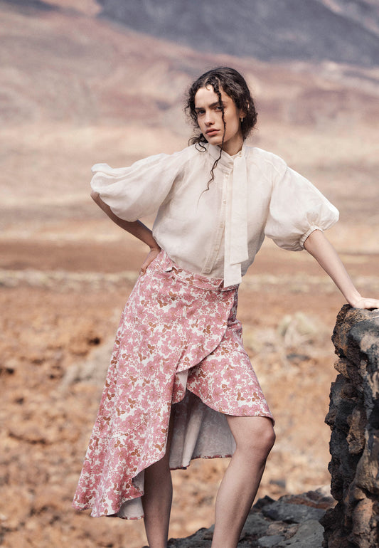 A model leaning against a rock wearing the NIIAM printed skirt and the AZALEA floral shirt.