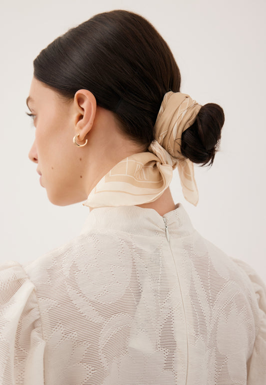 Close-up of the model’s hair tied in a sleek bun with the beige ARIA silk scarf wrapped around it.
