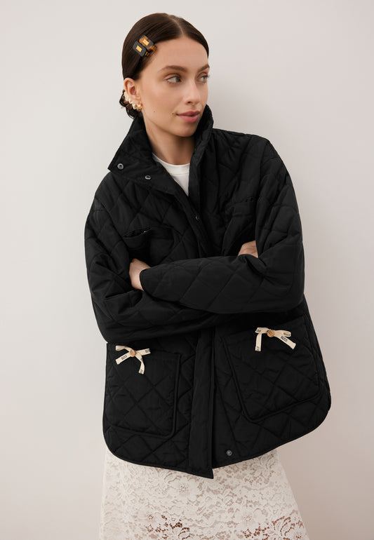 The front of the black NAYLA quilted jacket with decorative bows on the pockets.