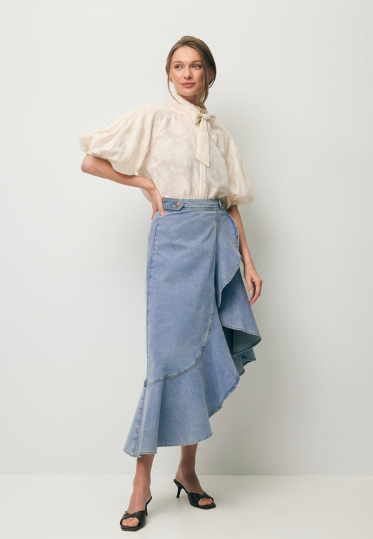 A model standing at an angle wearing the NIIA denim skirt with a decorative ruffle and the AZALEA floral shirt in cream.