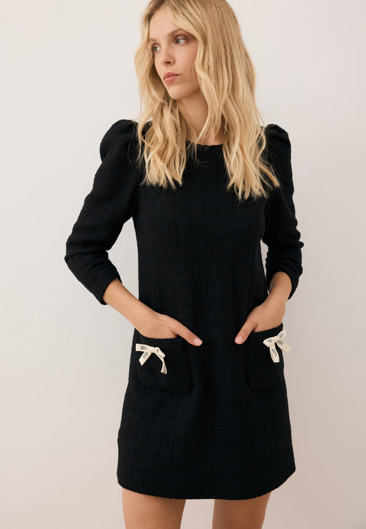 Model with hands in the pockets of the NOILLY dress, featuring branded bow details.