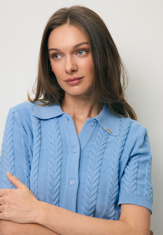 Close-up of a model with her hand in the pocket of the cream NUBE skirt, wearing the blue PATRI short-sleeved sweater with a collar.