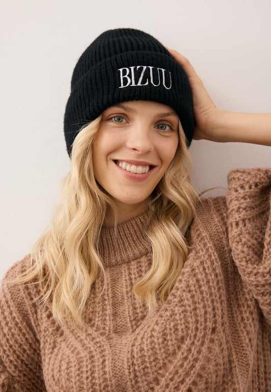 Close-up of the smiling model wearing the black ROYU merino wool beanie with a white embroidered logo.