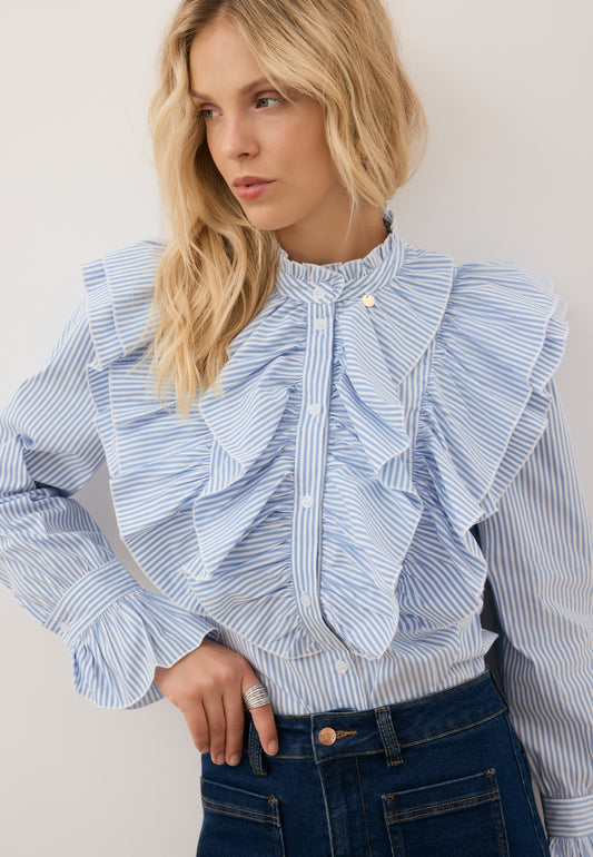 Close-up of a model with her hand in her jeans pocket, close-up of a blue shirt with decorative frills SANNI.