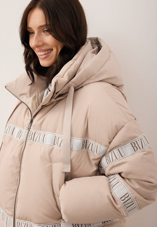 Close-up of a smiling model with her hand in the pocket, wearing the beige TOKYO jacket with natural filling, decorative stripe, and hood.