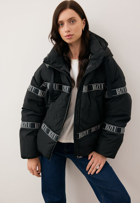 Model wearing an unzipped black down jacket with a branded TOKYO stripe.