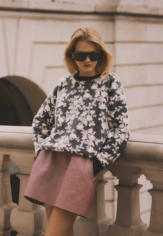 Model leaning against a wall wearing the floral CANELA sweater paired with the burgundy BREDA mini skirt.