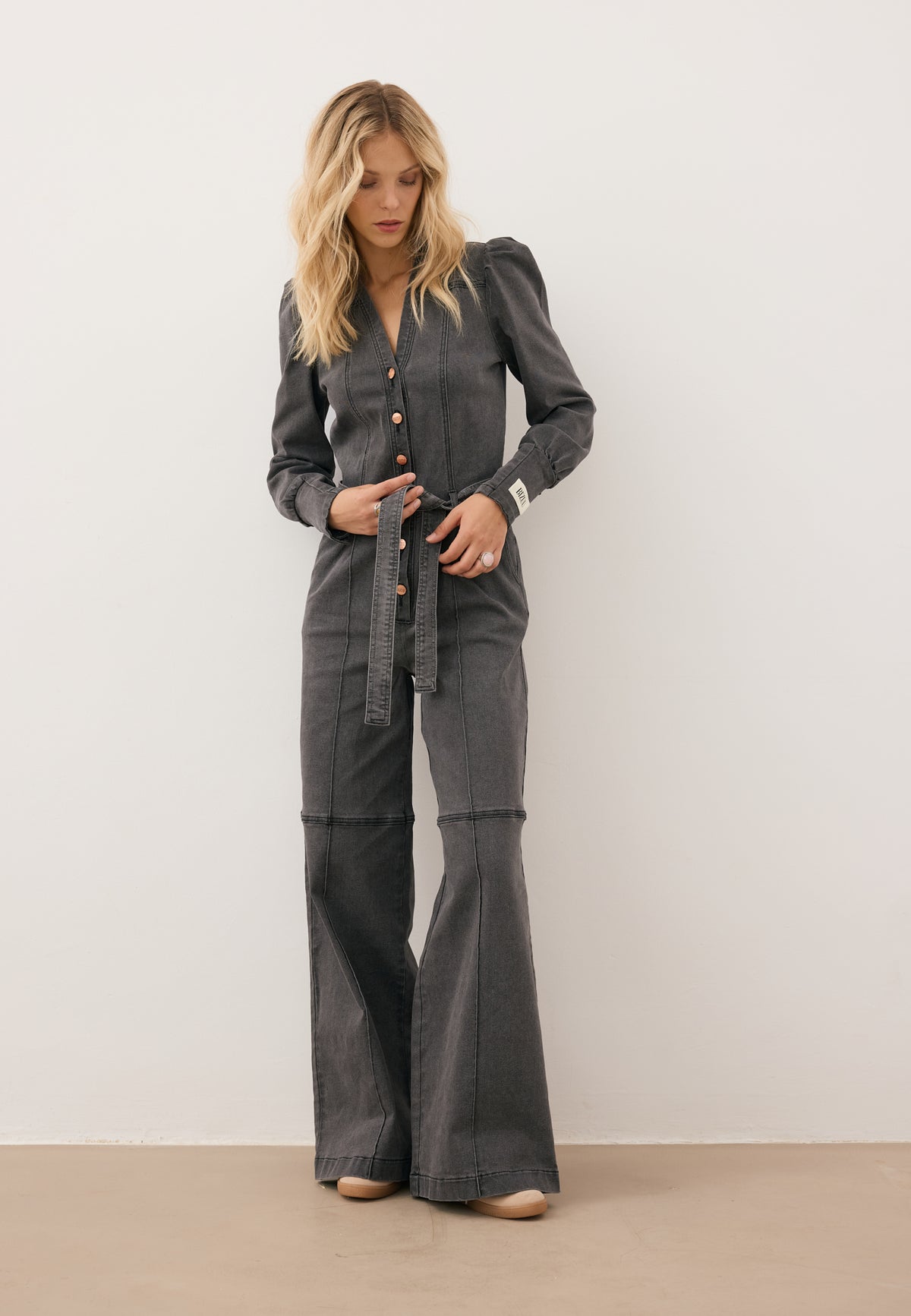The model is wearing a dark gray denim jumpsuit with a tie at the waist.