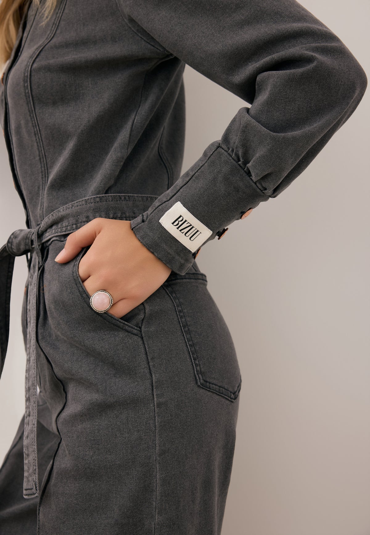 Close-up of the sleeve with the Bizuu logo on the dark gray MENDINA jumpsuit tied at the waist.