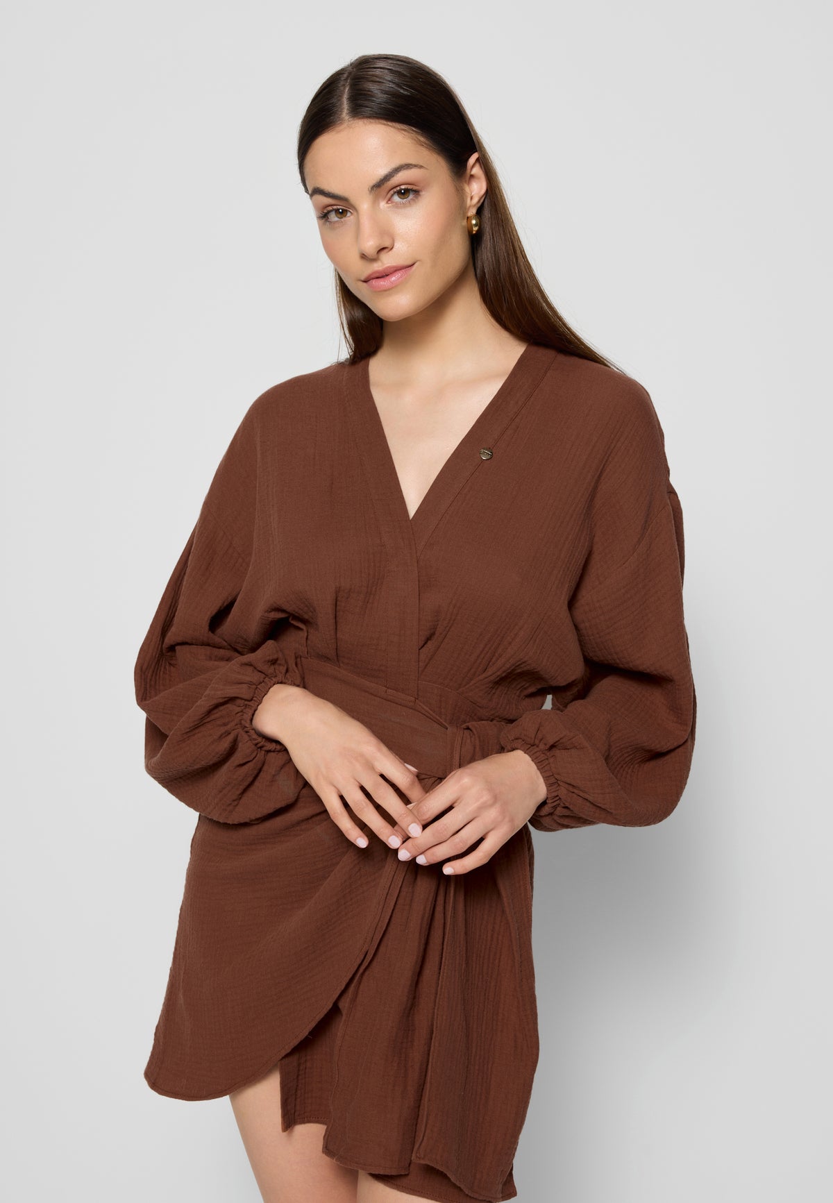 Model against a white wall in a brown MOULINS muslin dress.