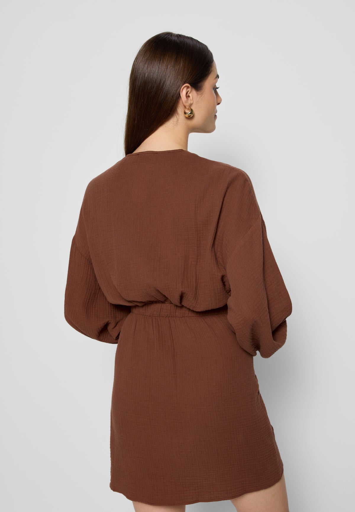 Model standing backwards in a brown MOULINS muslin dress.