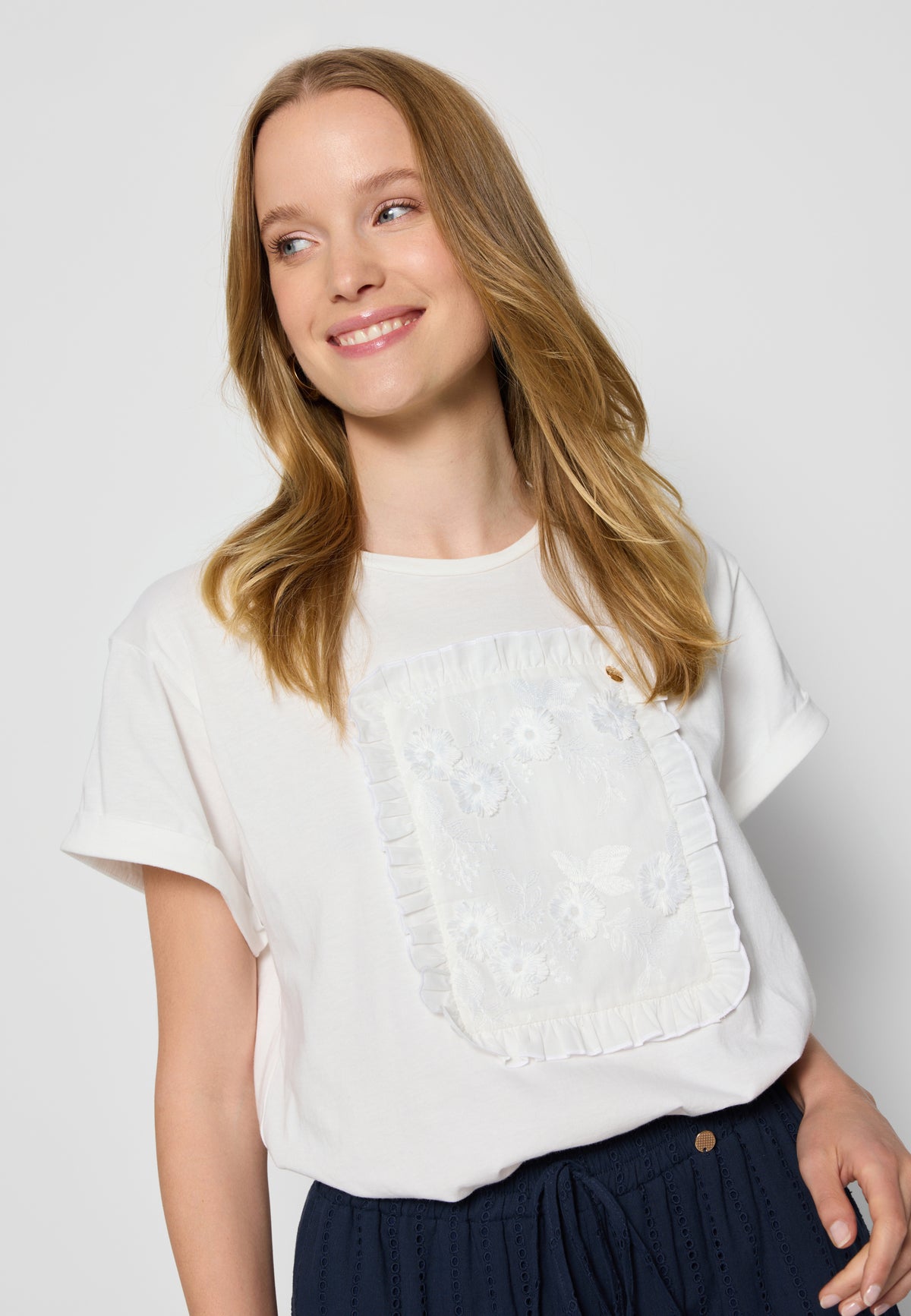 Close-up of a cream T-shirt with a floral MIRADO applique on the model.