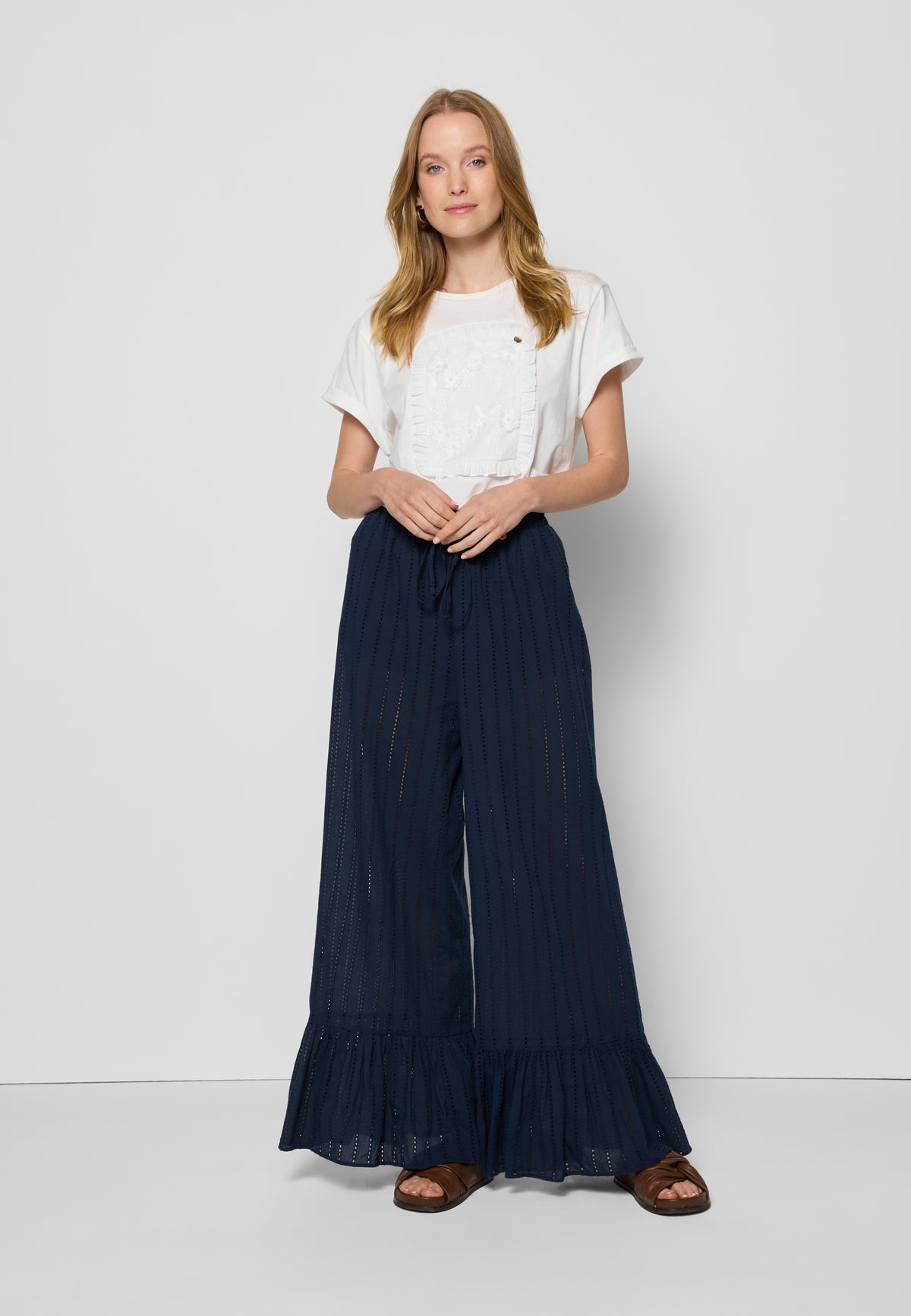 Model in white background wearing cream T-shirt with floral applique and navy blue LAVENDOU frill pants.
