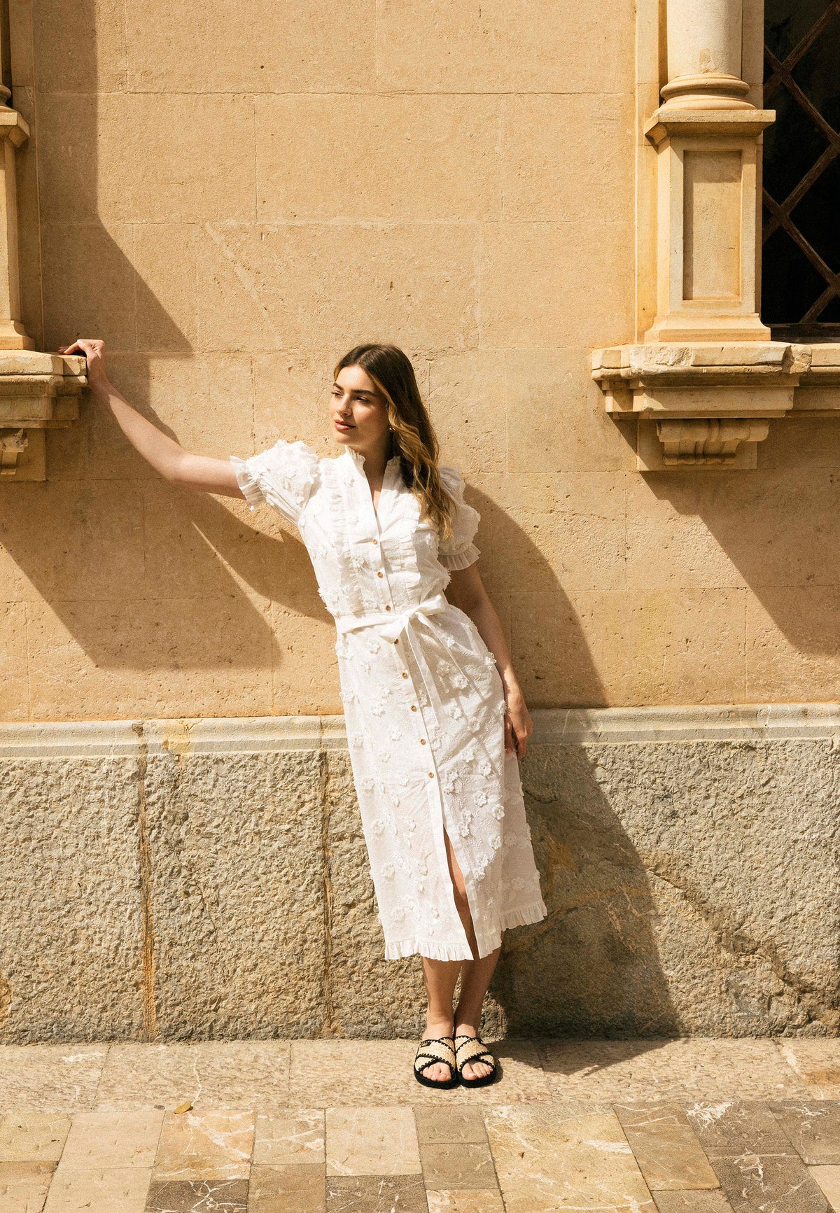 The model leaned with one hand against the windowsill wearing a white dress with a NATTA emery cut.