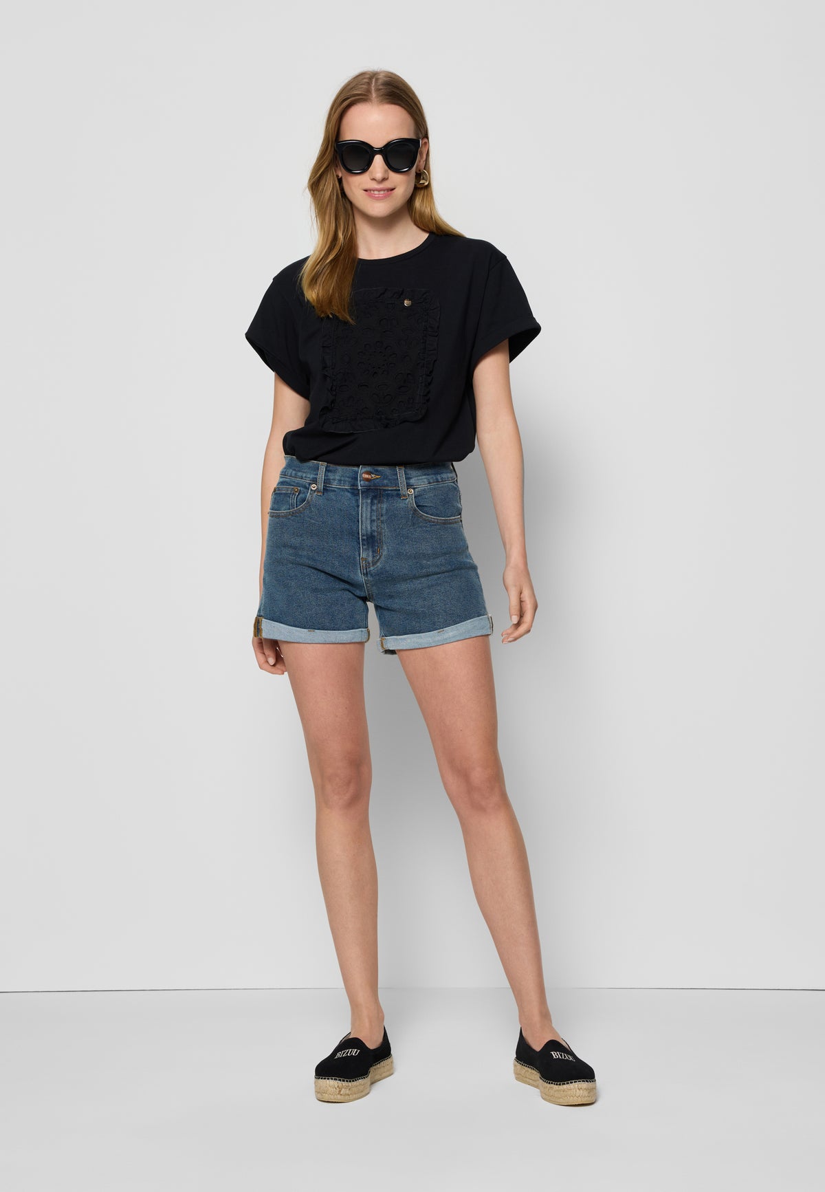 The model in white wearing MONREALE sunglasses, a black MIRADO T-shirt, MENORCA denim shorts and AYLA logo espadrilles.