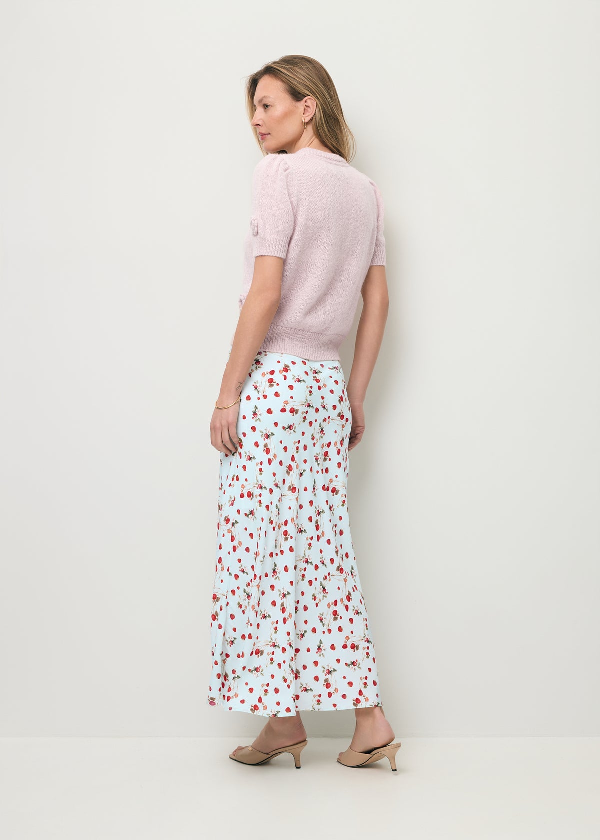 A model standing with her back to the camera, wearing a pink ADRIS short-sleeved sweater and a MOLLENA midi skirt.