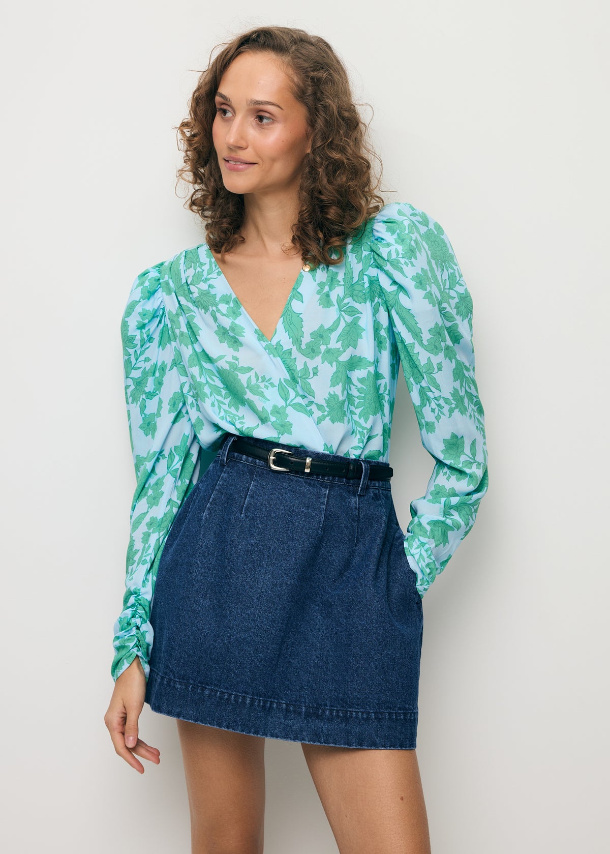 A model with her hand in the pocket of the BEDA denim skirt, wearing a wrap-style ALIBA bodysuit.