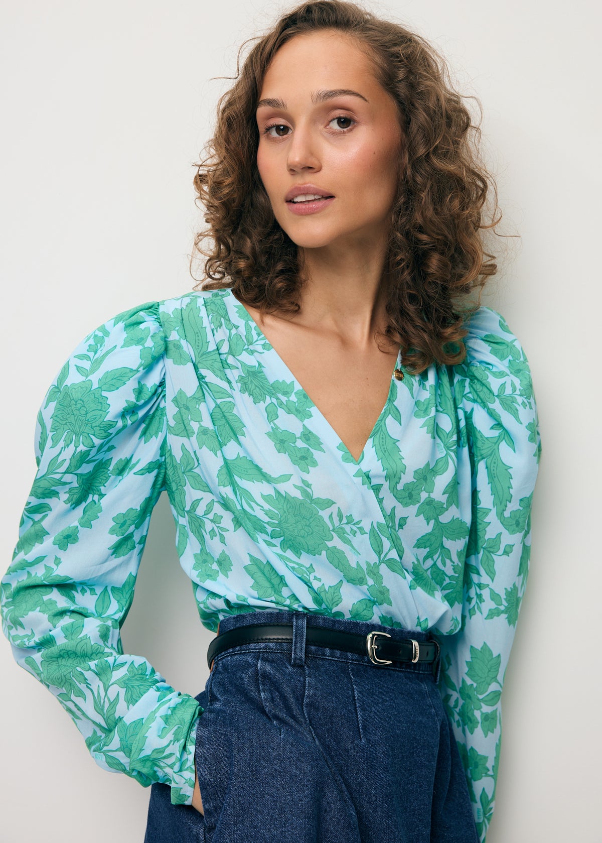 Close-up of a model wearing a blue bodysuit with an original ALIBA print and a BREDA denim mini skirt.