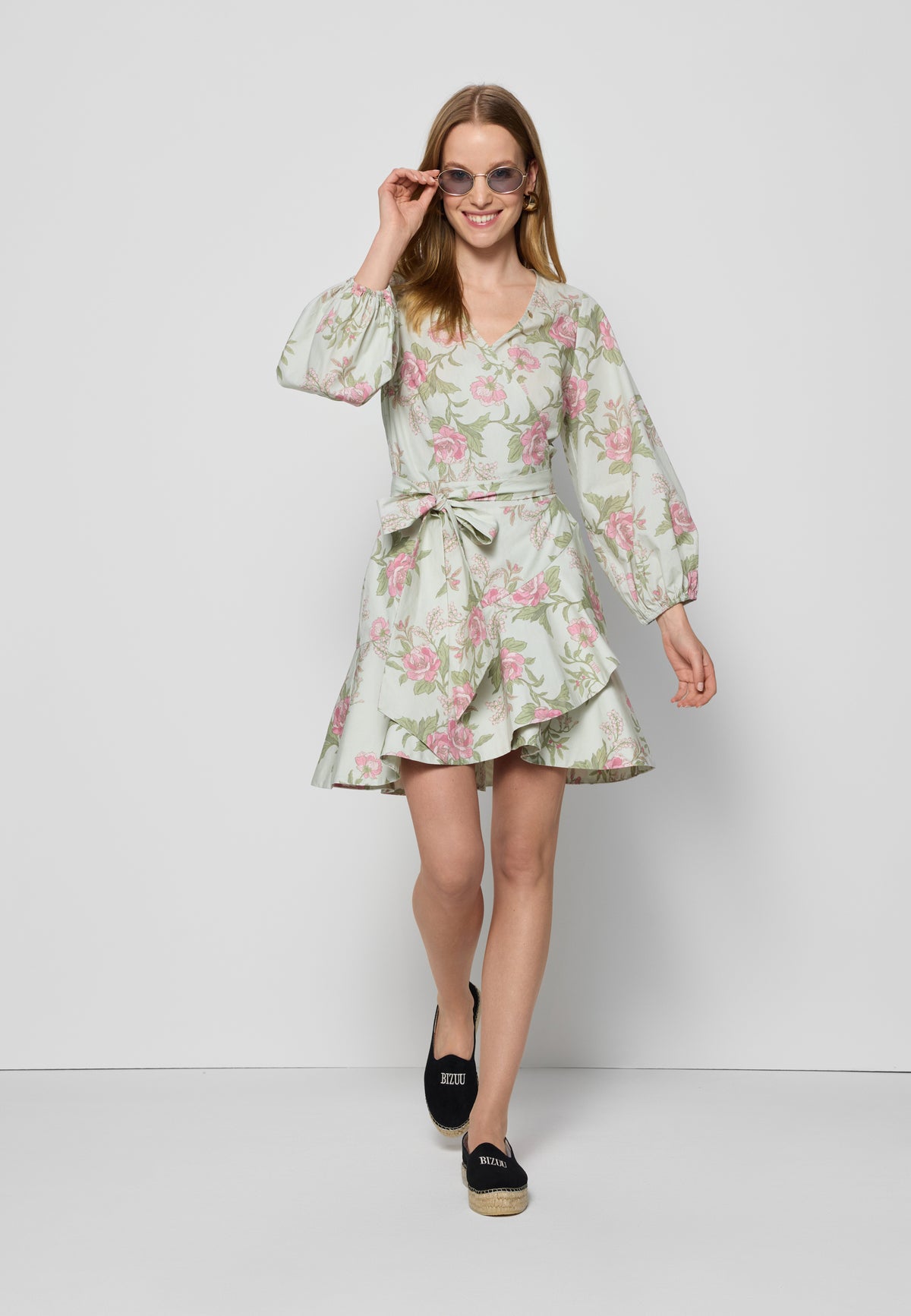 Model in AMBROSIA floral dress with envelope neckline and ruffle, wearing BIZUU logo espadrilles and sunglasses.