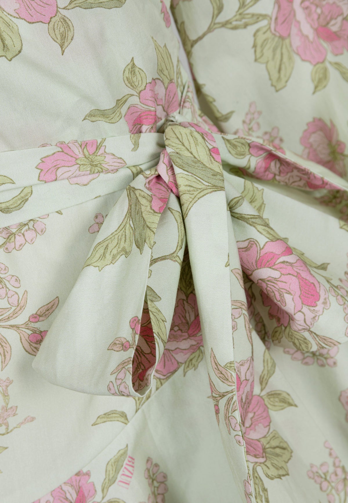 Close-up of the binding and pink floral print on the green background of the AMBROSIA dress.