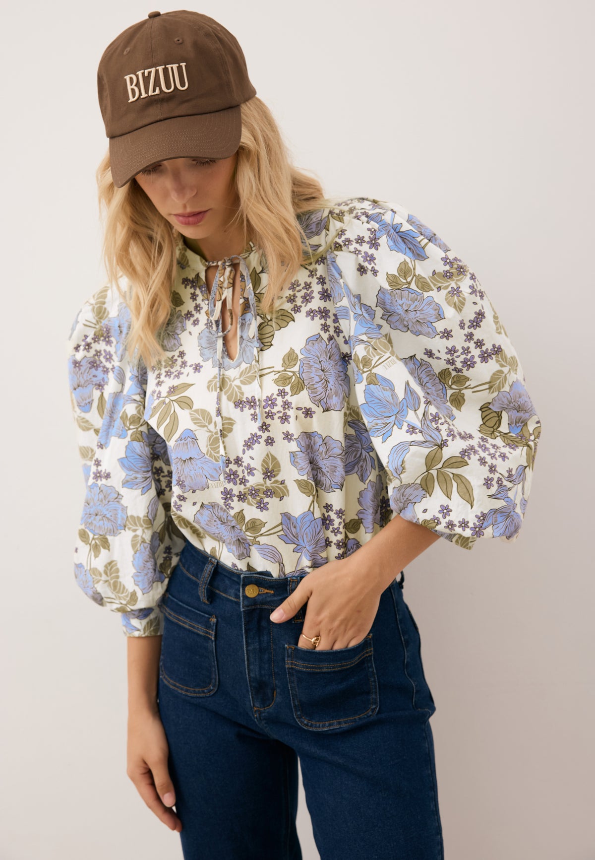 Model looking down with one hand in the pocket of her jeans, wearing the brown ZANE cap with embroidered logo.