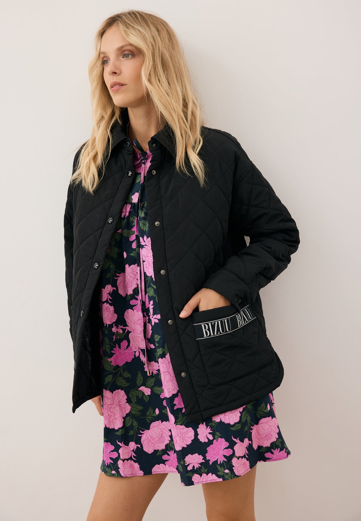 A model leaning against a wall with one hand in the pocket of a black MARIN quilted jacket.