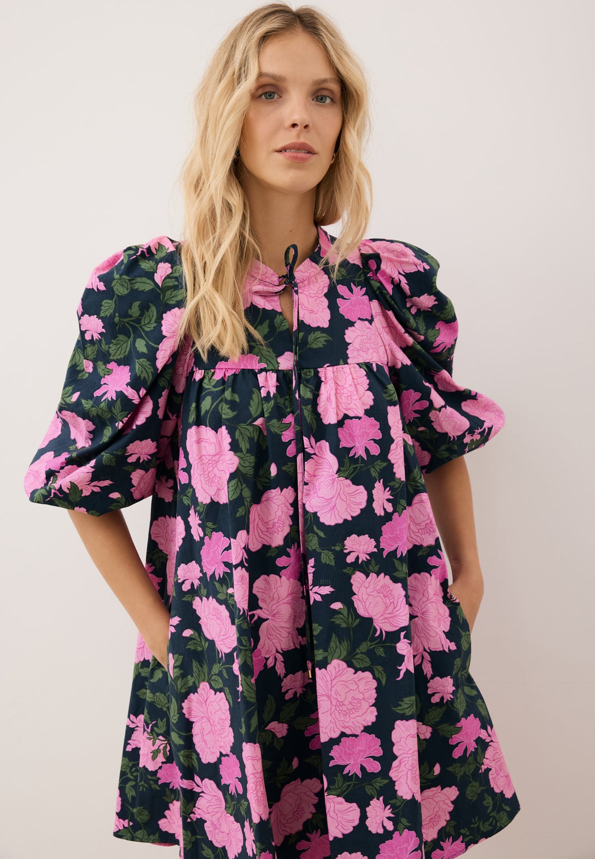 Close-up of a model holding her hand in the pocket of a loose-fitting AYOTE mini dress.