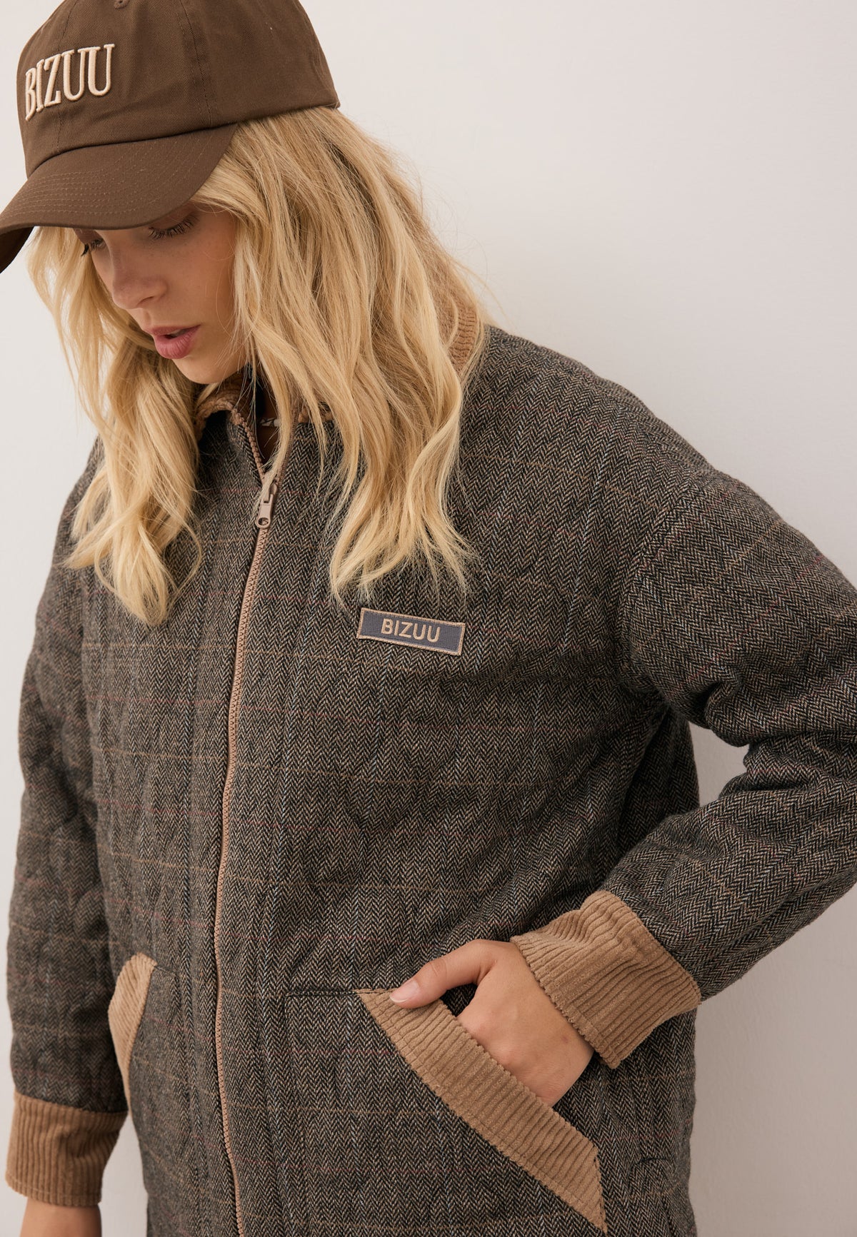 Model wearing the BAIONE jacket with one hand in the pocket, styled with the brown cotton ZANE cap featuring front logo.