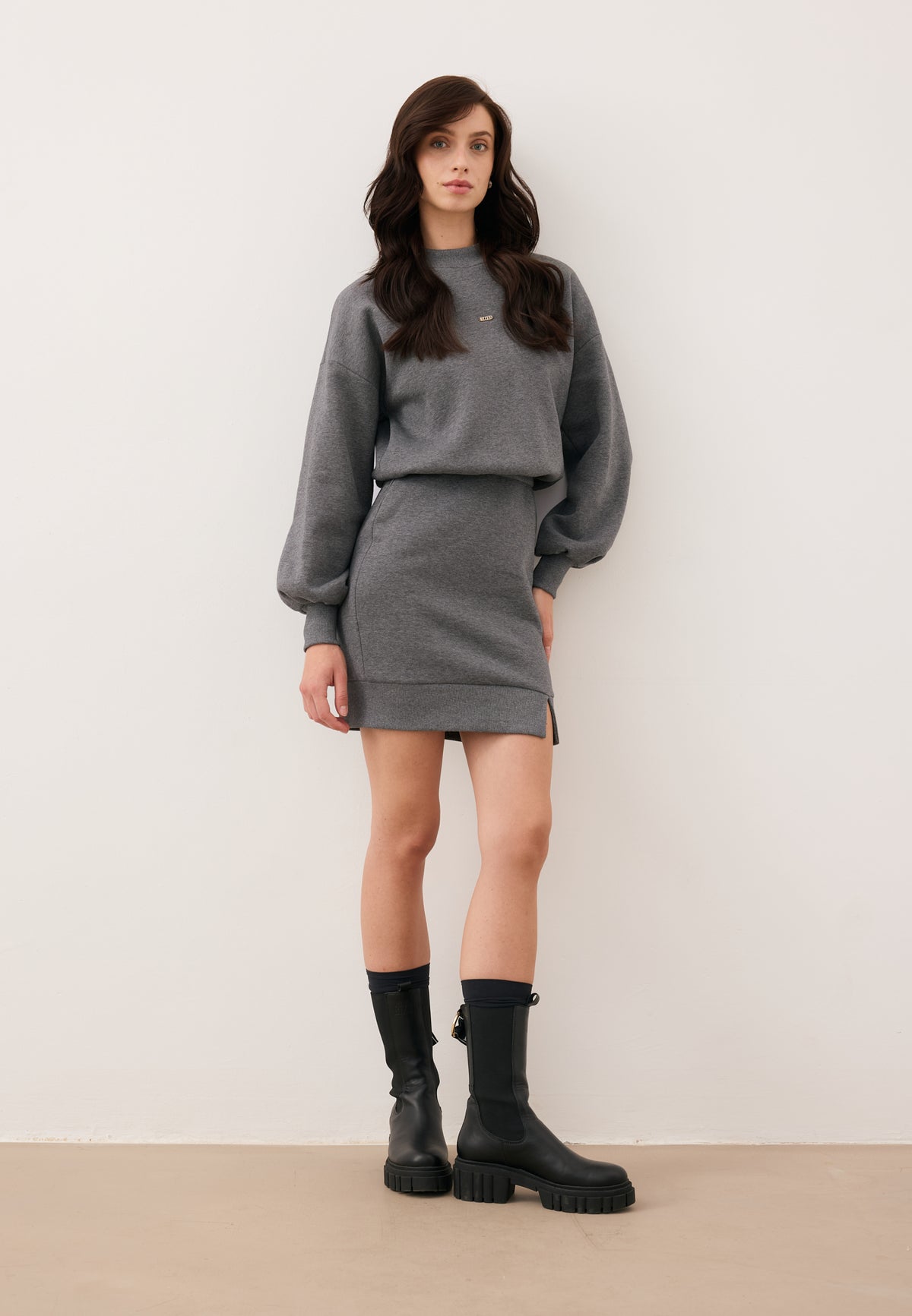 Model leaning against a wall, dressed in the CAGLIARI knit mini dress paired with TORIDE ankle boots.