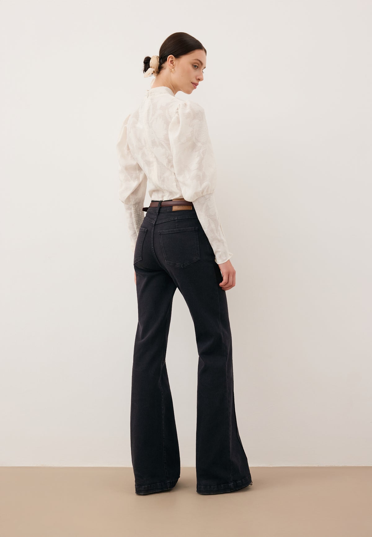 Model standing sideways wearing black BELINNA flare jeans and a cream DEFIORI bodysuit.