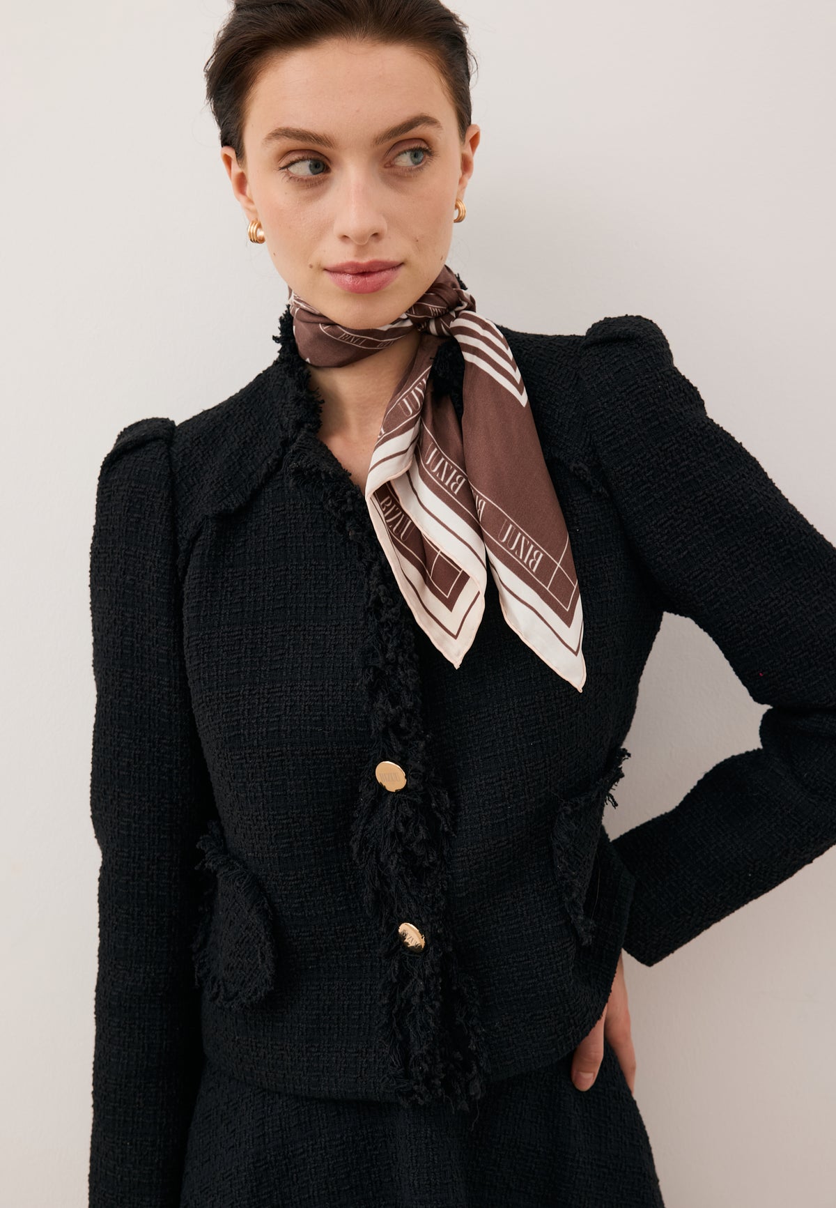 Close-up of the model wearing the black DITAS blazer with gold buttons, styled with the ARIA brown silk scarf.