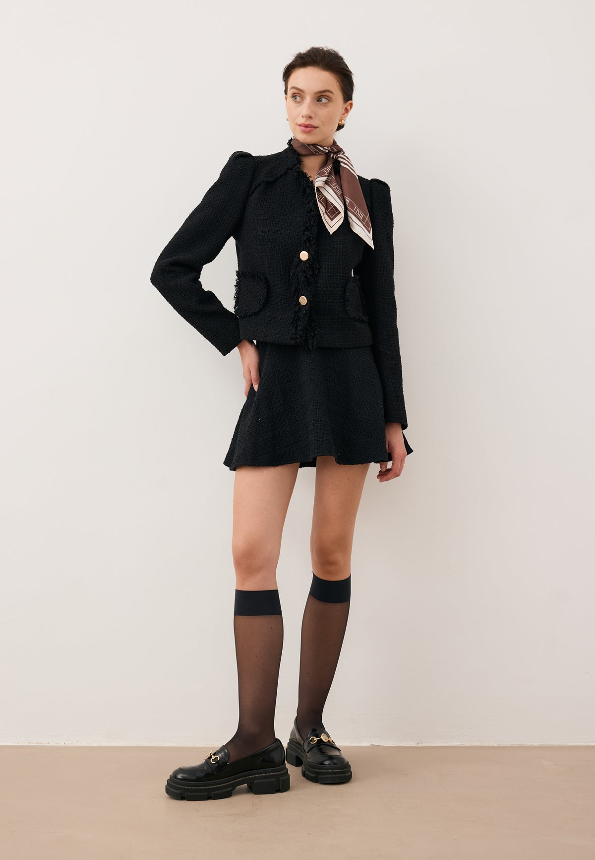 Model with one hand on her hip, dressed in the black WENDYS mini skirt and cropped DITAS jacket, accessorized with the ARIA silk scarf.
