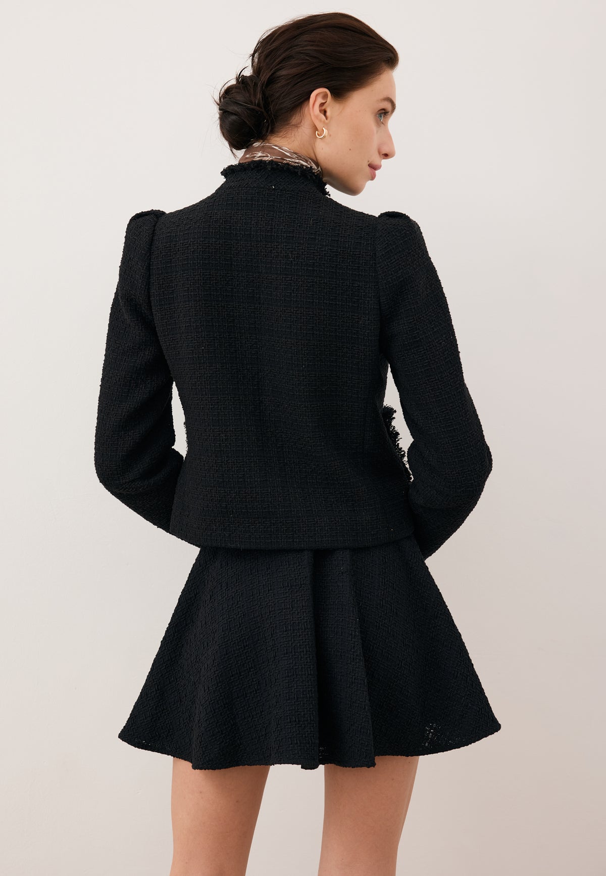 Model standing with her back to the camera, looking to the side, wearing the black set – DITAS blazer and WENDYS mini skirt.