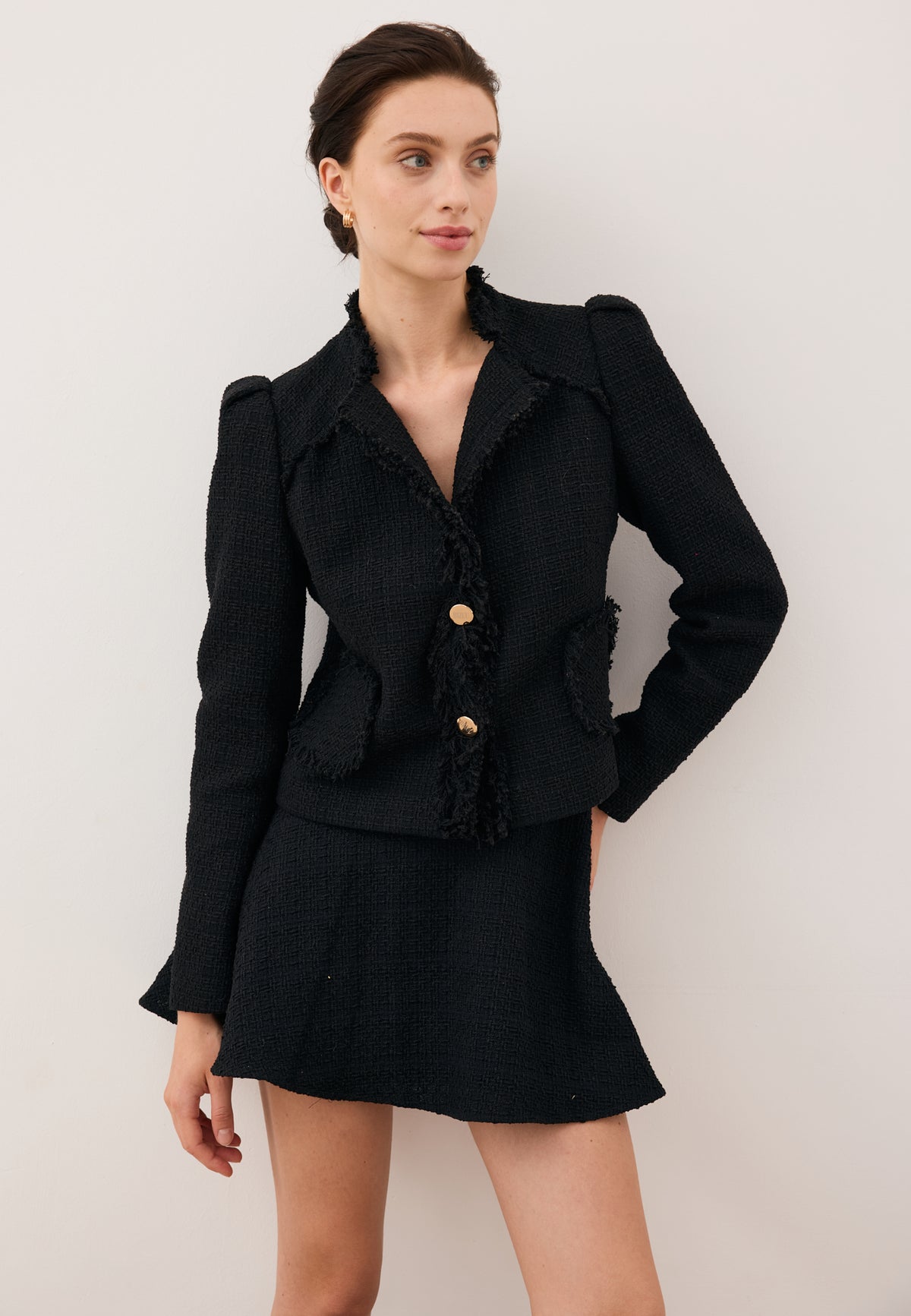 Model with one hand on her hip, looking to the side, dressed in the black DITAS blazer with decorative collar and gold buttons, paired with the WENDYS mini skirt.