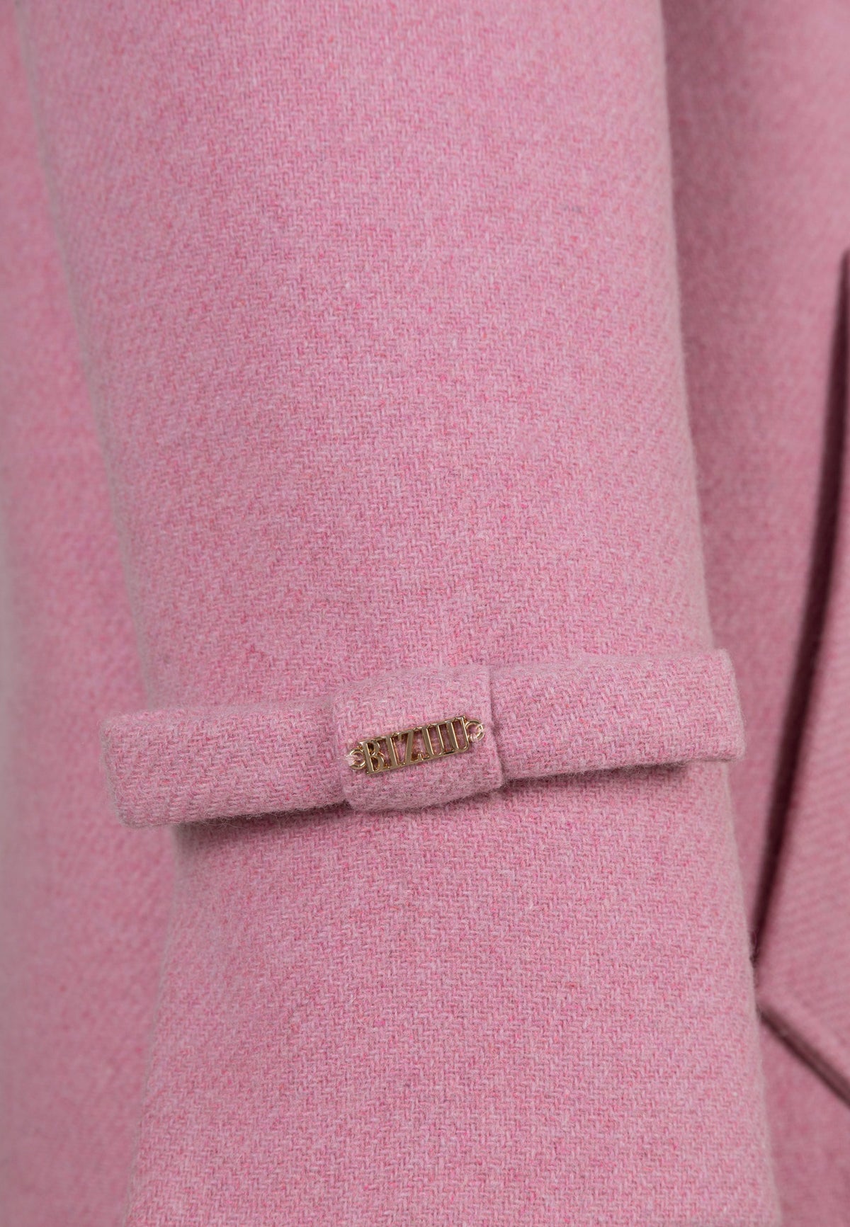Close-up of the bow with a gold logo decorating the sleeve of the ERICE coat.