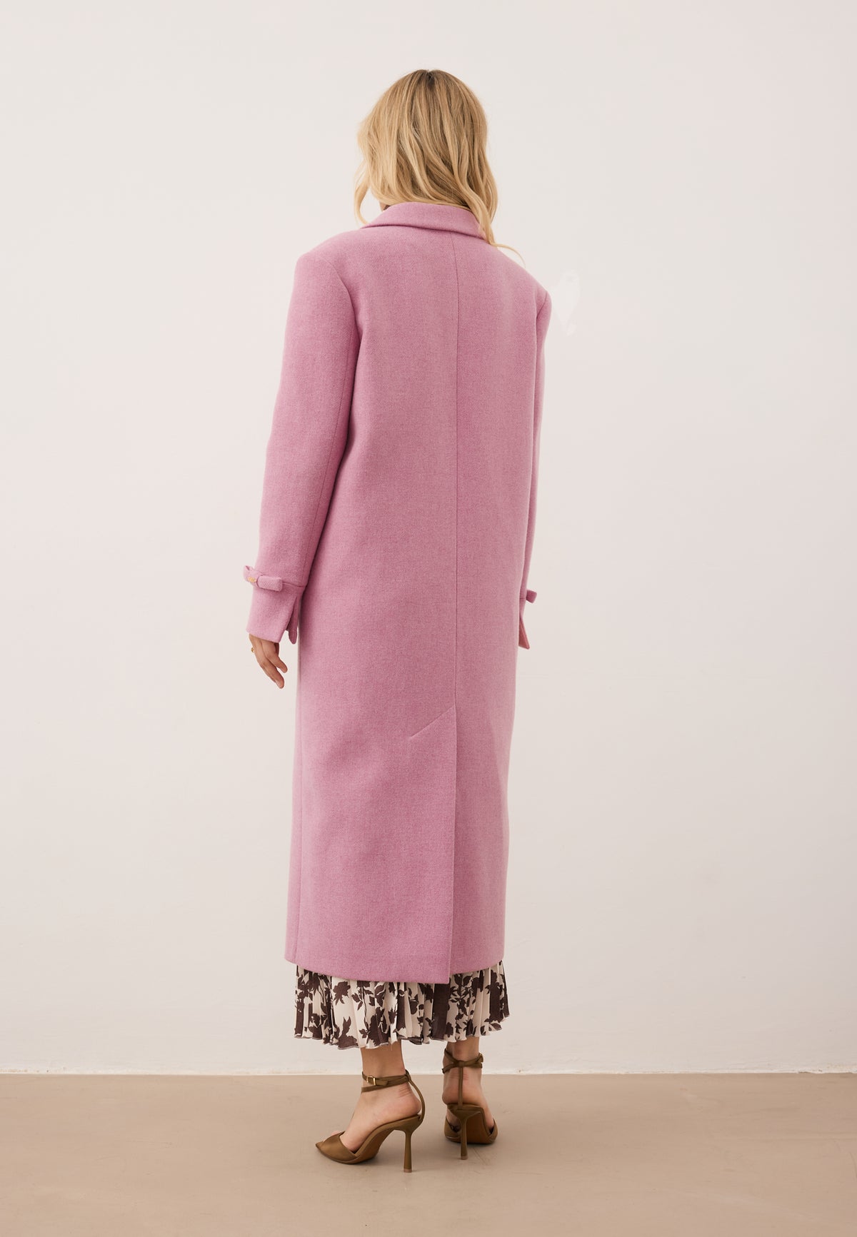 Model standing with her back turned in the pink ERICE coat with a classic, straight cut.