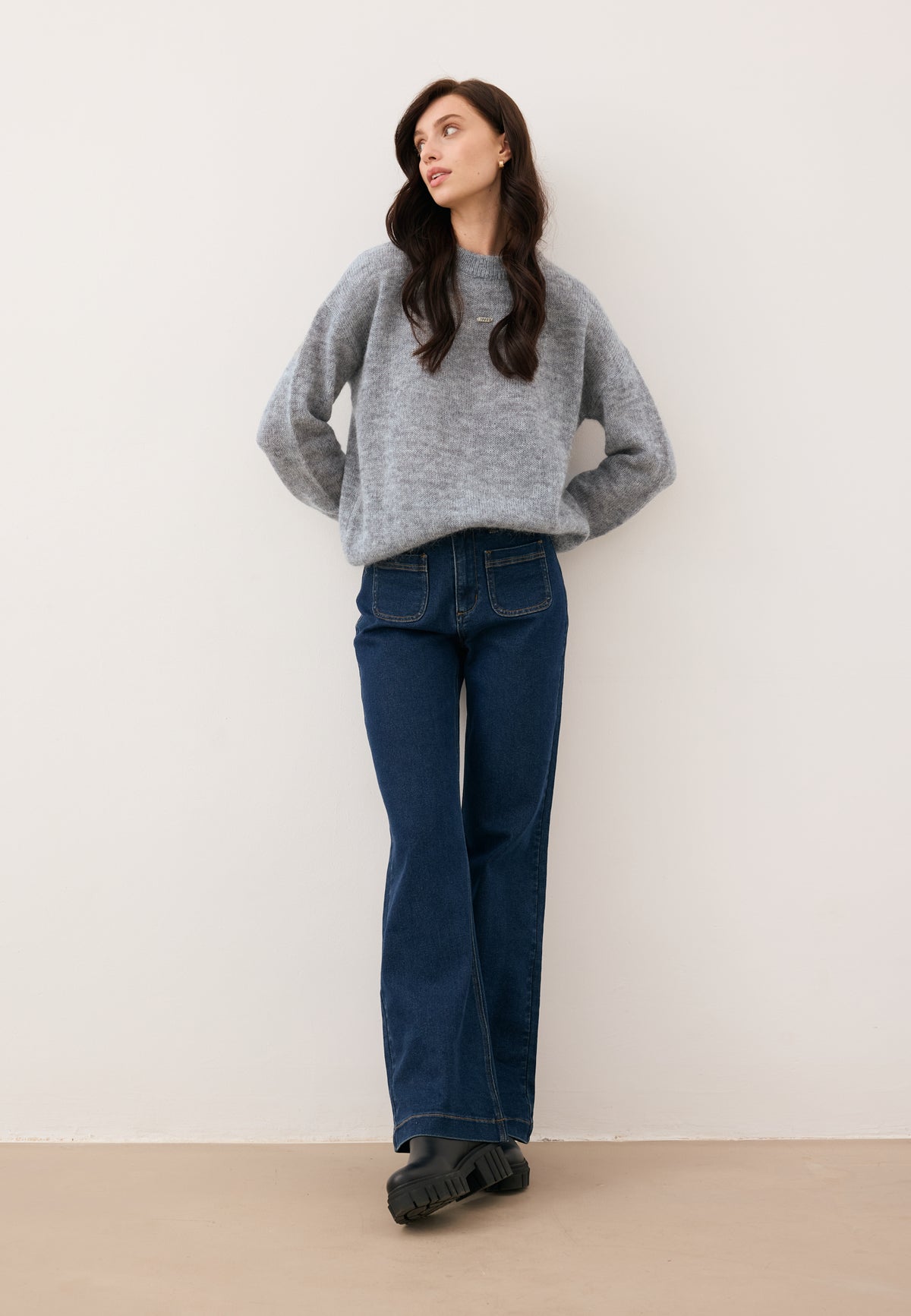 Model leaning against a wall, styled in the gray wool FAROA sweater and navy DELPHI jeans.