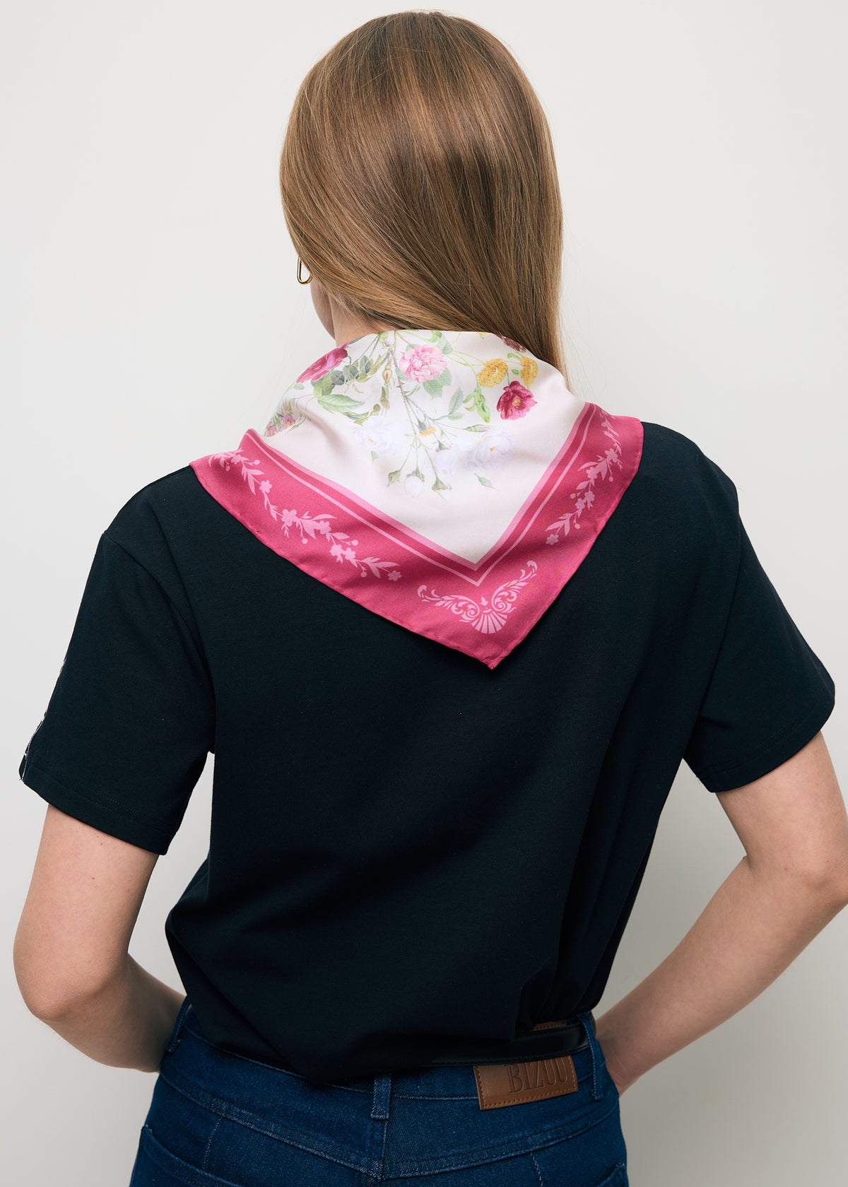 A pink silk FIORIA scarf folded into a triangle and tied, showing how it sits around the neck.