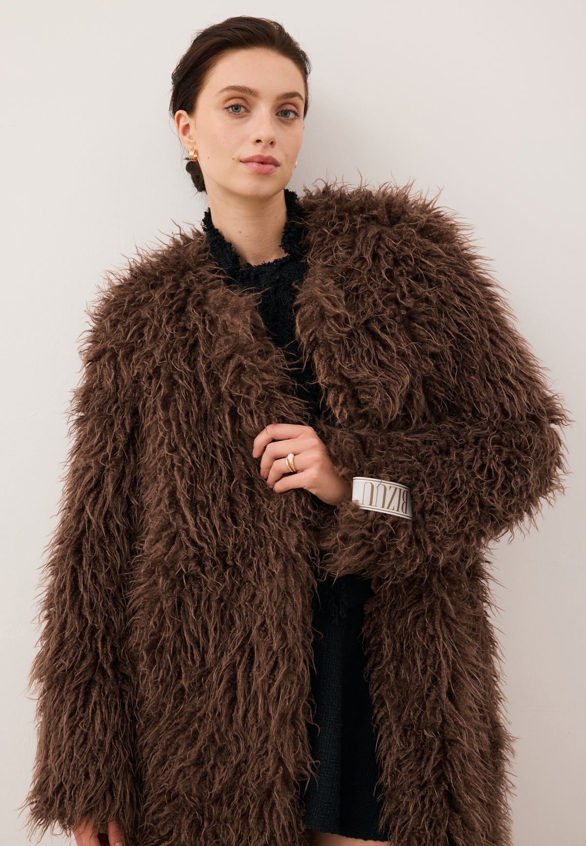 Close-up of the model holding the collar of the unbuttoned GENUA coat, with the logo label visible on the sleeve.