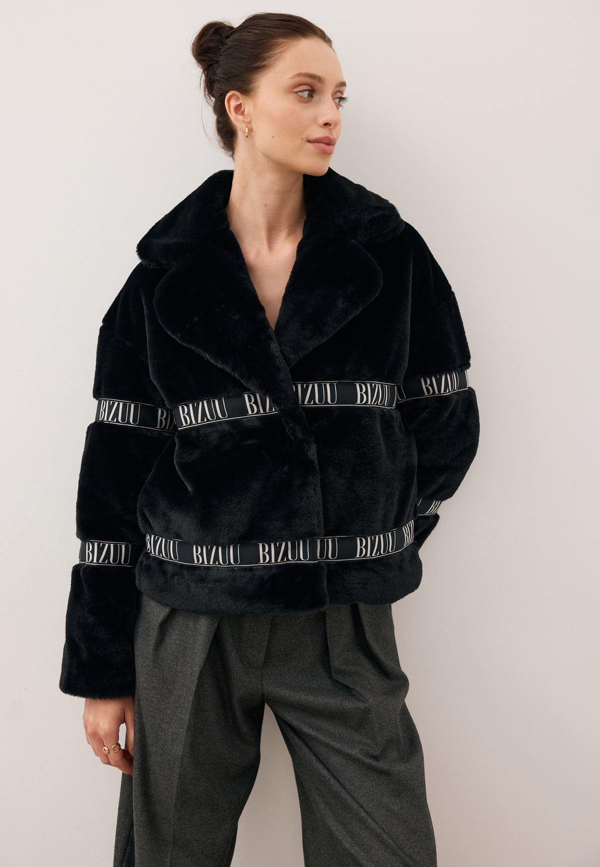 Model looking to the side with one hand behind her back, wearing the boxy black GREGORIA faux fur coat.