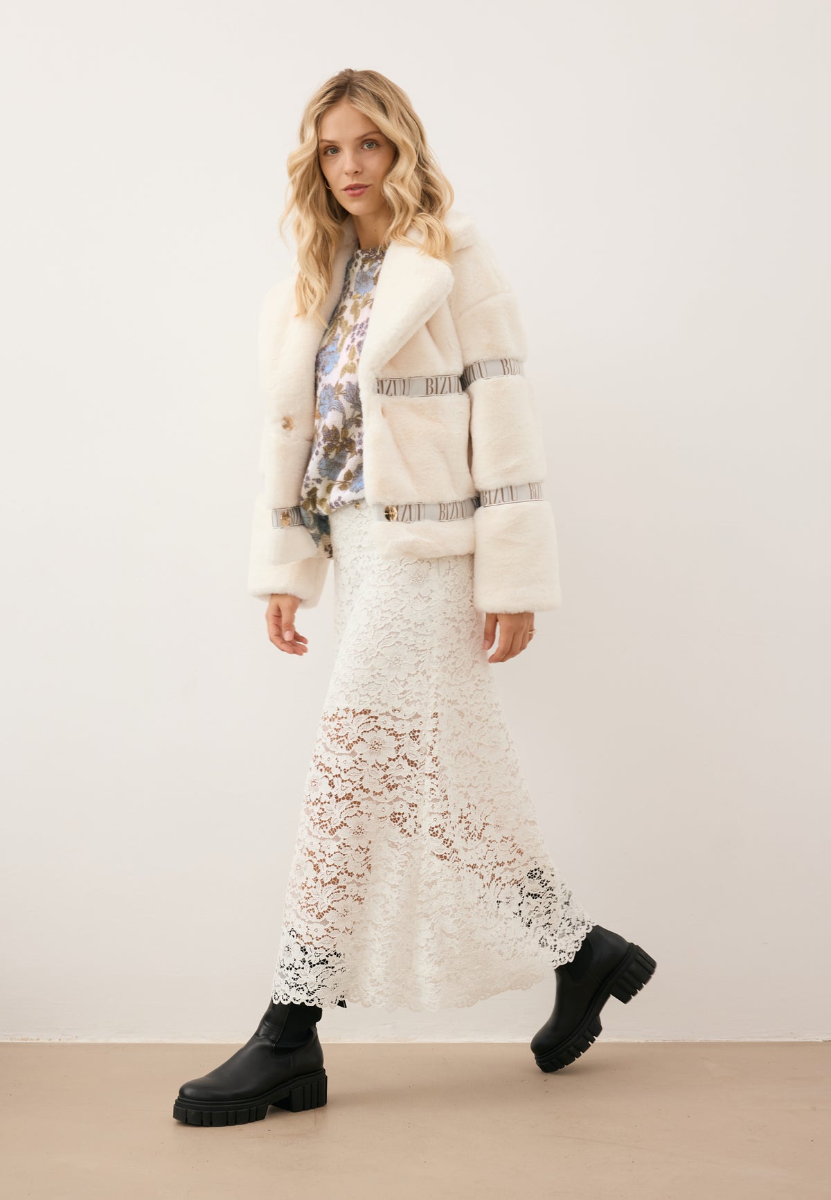 Model stepping forward, styled in the cream GREGORIA coat, MENTON sweater, MILKY skirt, and TORIDE ankle boots.