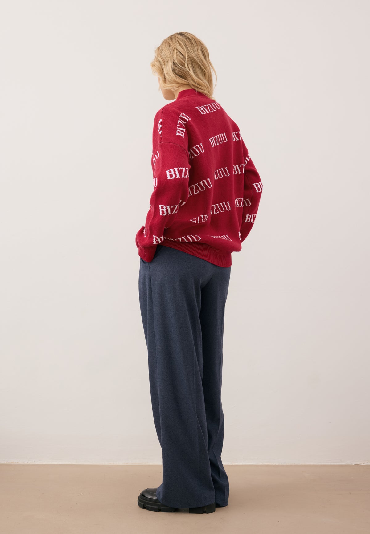 Model standing with her back to the camera wearing the burgundy KYLE logo sweater and navy BANOS wide-leg trousers.