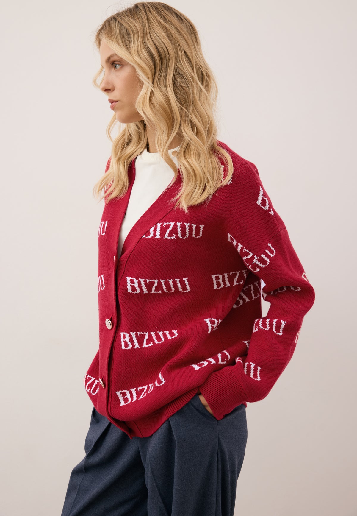 Model standing sideways with one hand in the pocket of navy BANOS trousers, wearing the burgundy KYLE sweater.