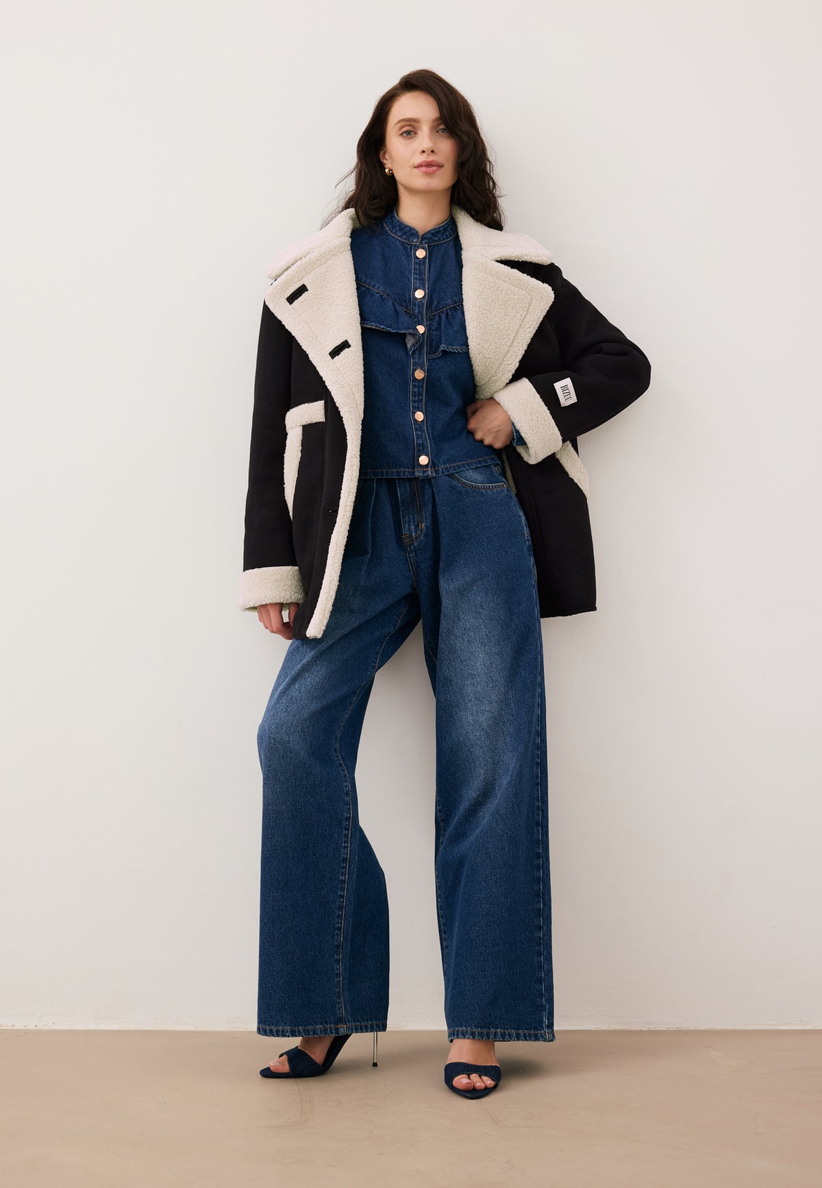 Model in an unbuttoned black LAFARA shearling jacket, styled with the denim DILETTA and LEYLA set.