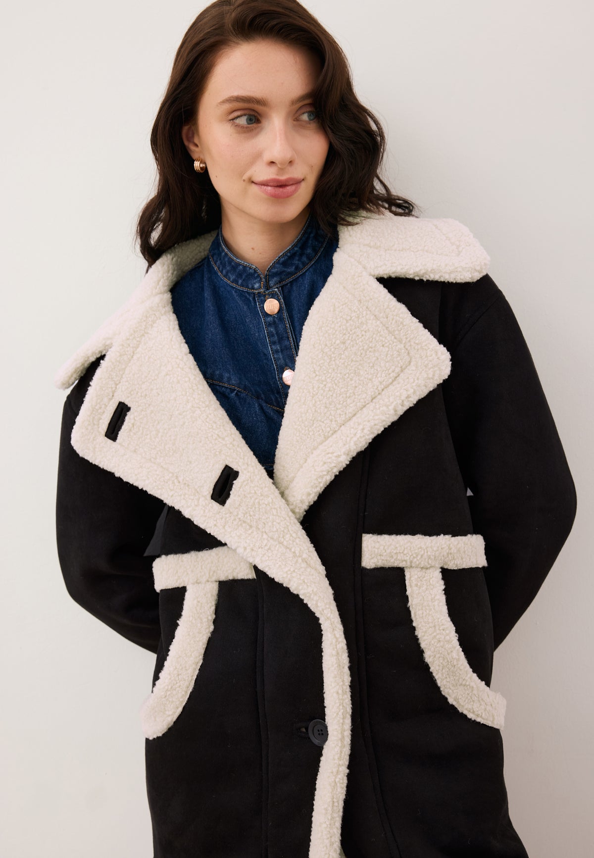 Close-up of the model with her hands behind her back, wearing the black eco-shearling LAFARA jacket.
