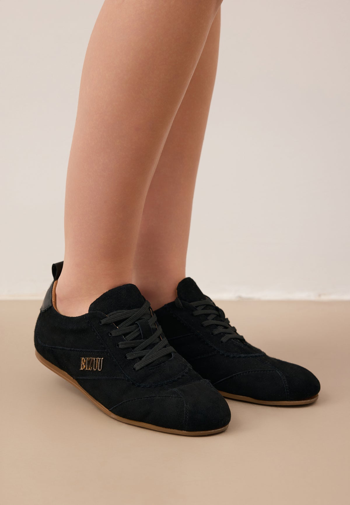 Close-up of the model's legs in black suede LEOLA sneakers with a gold logo on the side.