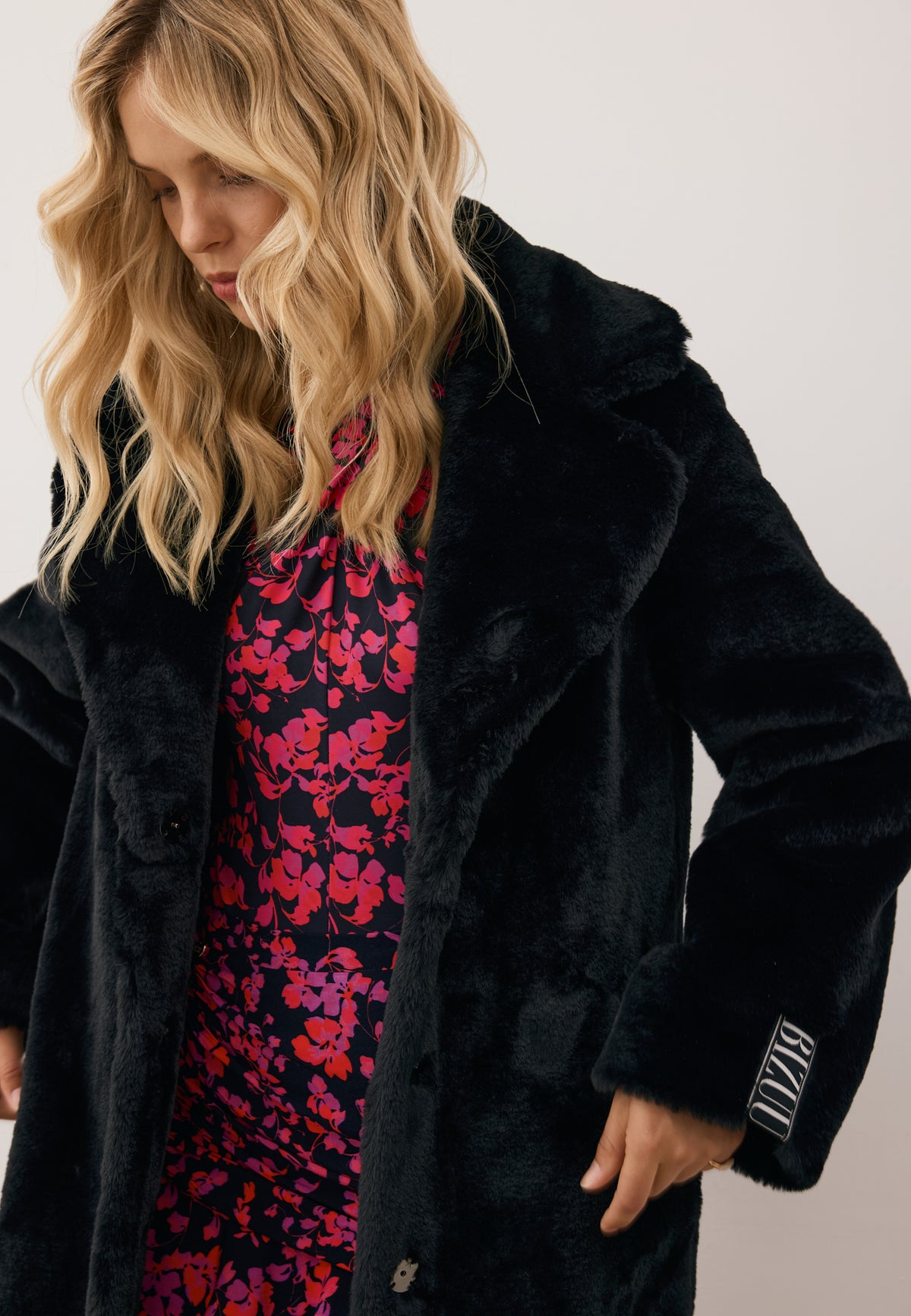 Close-up of the model wearing a black LIVORNO fur coat with a branded label on the sleeve.